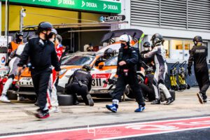 Im hektischen Boxenstopp arbeiten mehrere Mechaniker an einem orange-weißen GT-Rennwagen mit Startnummer 311 unter DEKRA- und FK-Performance-Bannern.