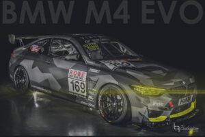 Zu sehen ist ein grau getarnter BMW M4 EVO Rennwagen mit ROVE-Motoröl- und H&R-Decals, gelben Akzenten und Startnummern.