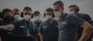 Mehrere Teammitglieder von FK Performance mit Headsets und weißen Schutzmasken, im Motorsport-Teamwork während der Fahrerkommunikation.