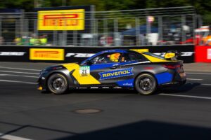 Rennwagen mit gelber und blauer Ravenol-Lackierung fährt auf einer Rennstrecke.