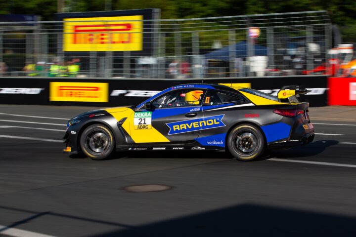 Rennwagen mit gelber und blauer Ravenol-Lackierung fährt auf einer Rennstrecke.