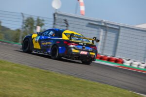 Blauer und gelber Rennwagen mit Sponsorenlogos, der auf einer Rennstrecke fährt.