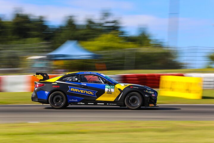 Schwarzer Rennwagen mit blauen und gelben Akzenten fährt auf einer Rennstrecke.
