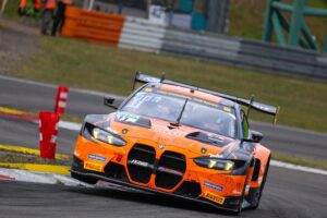 Schwarzer und orangefarbener BMW Rennwagen während eines Rennens auf der Strecke.
