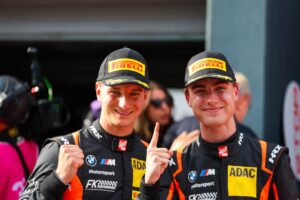 Zwei Rennfahrer in Pirelli-Caps und ADAC-Motorsportanzügen zeigen den Finger nach oben.