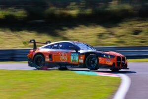 Rennwagen in Orange mit Startnummer 11 fährt mit hoher Geschwindigkeit auf der Rennstrecke.