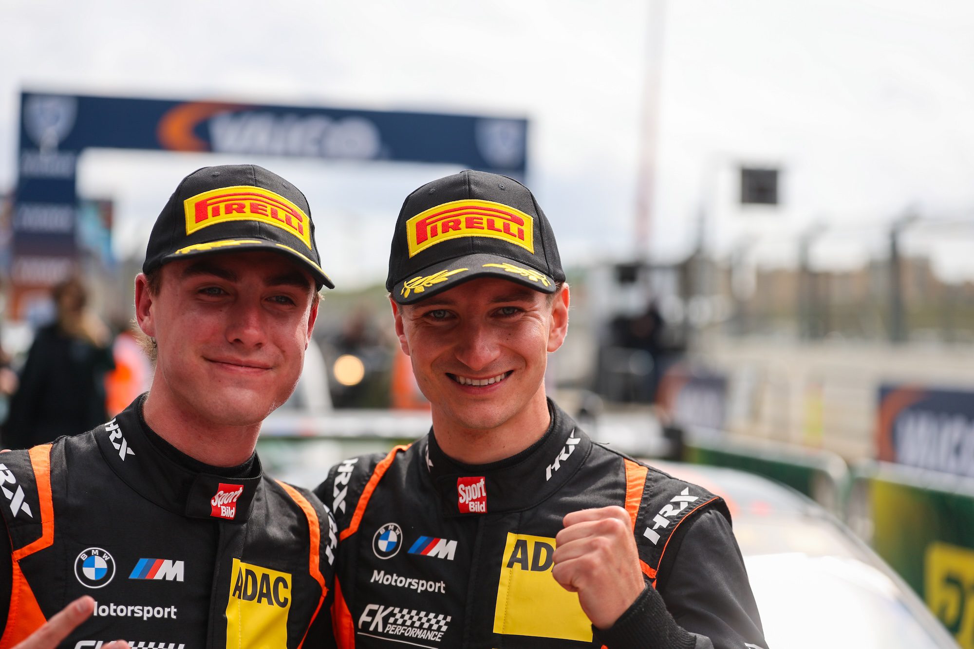 Zwei junge Rennfahrer in Pirelli-Caps posieren lächelnd nach einem Rennen.