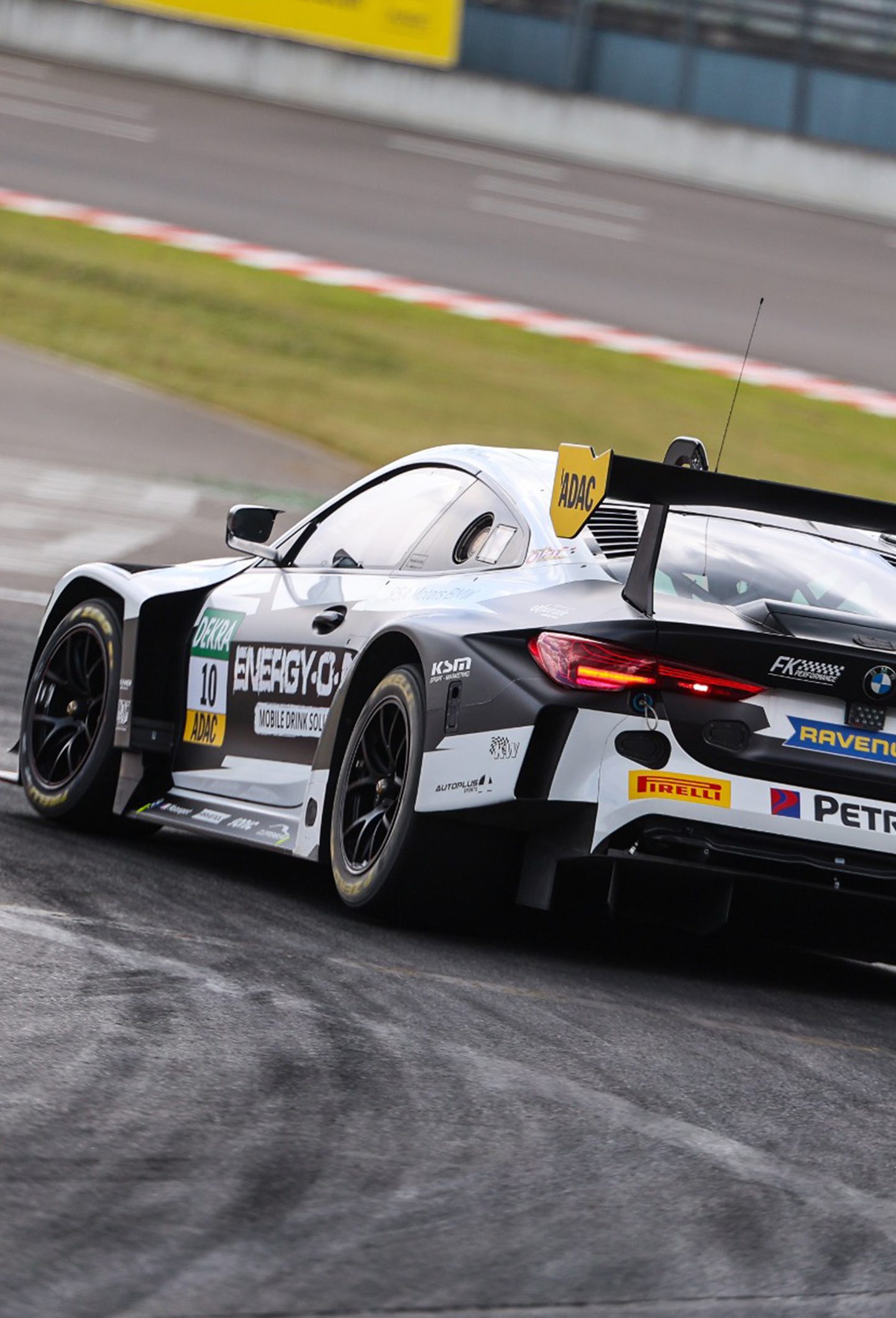 BMW M4 mit Startnummer 10 fährt durch eine Kurve auf der Rennstrecke, sichtbare Reifenspuren, Sponsorenlogos und großer Heckflügel.