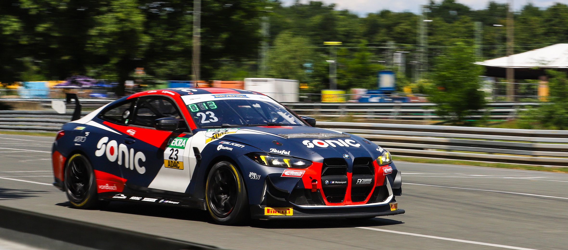 Rennwagen BMW M4 GT4 EVO, Startnummer 23 (Sylvestersson/Ellerine) in blau-rot-weißer Sonic-Lackierung, fährt auf Rennstrecke. ADAC GT4 Deutschland.