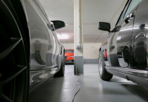 Nahaufnahme zwischen zwei glänzenden Luxusautos. Im Hintergrund roter Sportwagen und Ladekabel auf dem Boden.