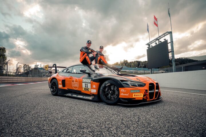 BMW M4 GT4 Rennwagen in Orange-Schwarz mit zwei Fahrern auf dem Dach auf einer Rennstrecke