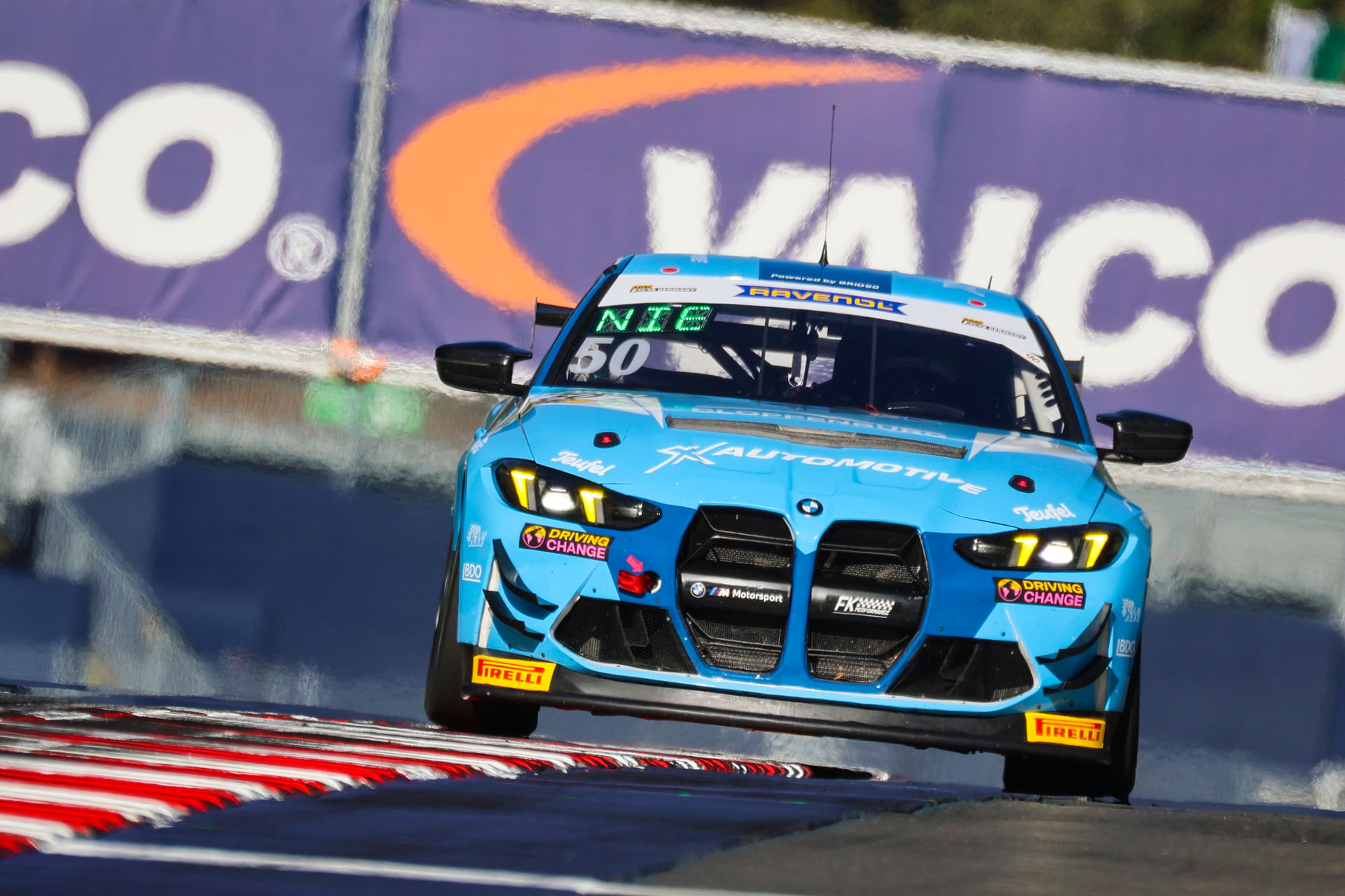 Frontalansicht des hellblauen BMW M4 GT4 (Startnummer 50) von FK Performance Motorsport auf der Rennstrecke vor einem VAICO-Banner.