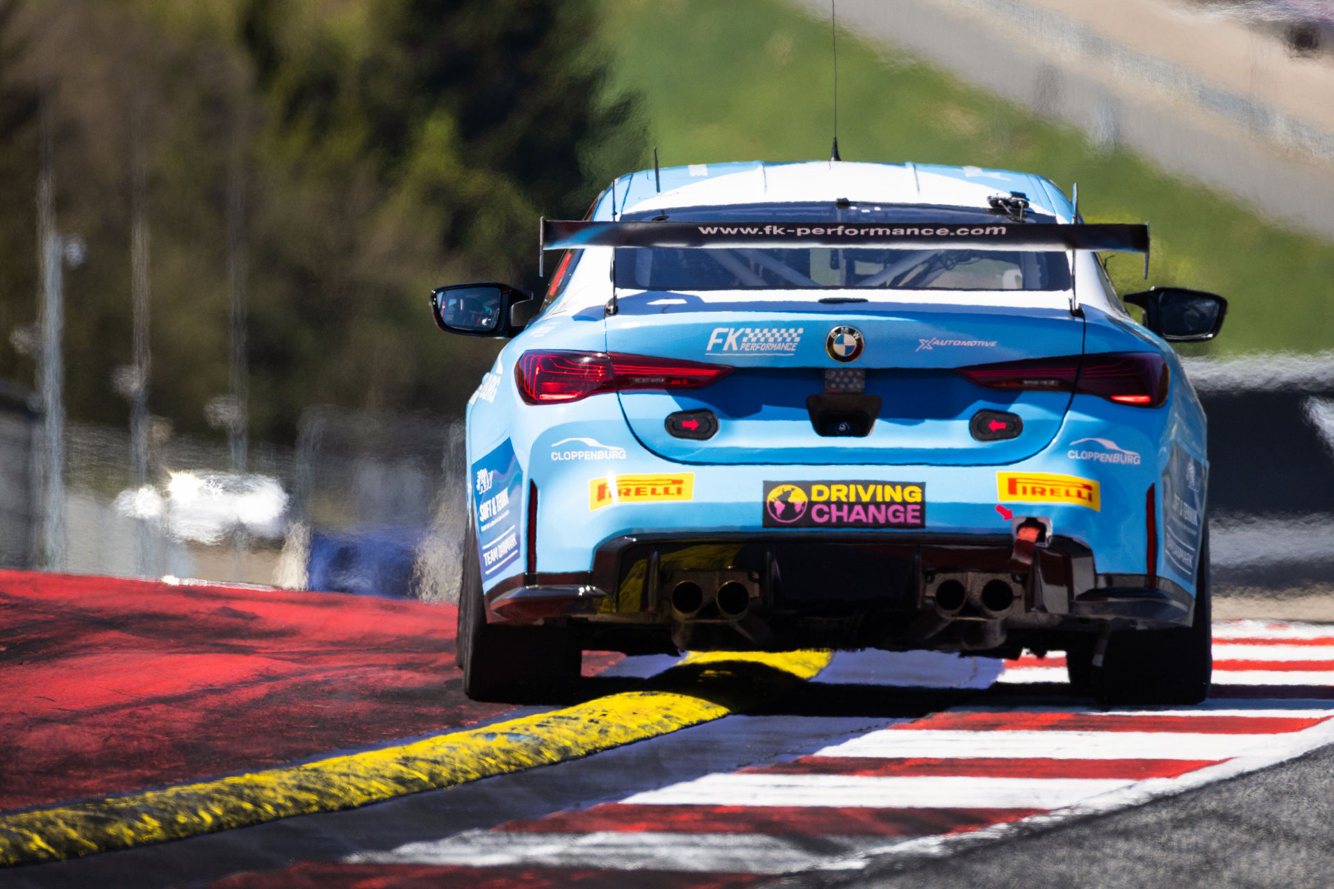 Heckansicht des hellblauen BMW M4 GT4 von FK Performance beim Überfahren der gelben Curbs am Kurvenausgang.