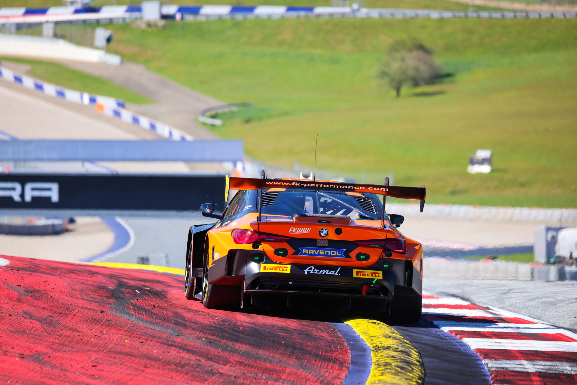 Heckansicht des orange-schwarzen BMW M4 GT3 von FK Performance Motorsport auf der Rennstrecke beim Überfahren der Curbs.