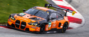 Seitliche Ansicht des BMW M4 GT3 im orange-schwarzen Industreer-Design während einer Kurvenfahrt auf der Rennstrecke.