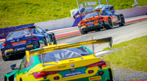 Drei BMW M4 GT3 Rennwagen von FK Performance Motorsport in Blau-Orange, Orange und Gelb-Grün hintereinander auf der Rennstrecke.