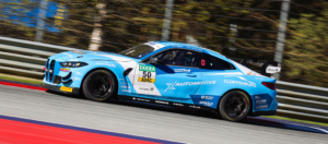 Seitliche Profilansicht des hellblauen BMW M4 GT4 im X-Automotive-Design während einer schnellen Fahrt auf der Strecke.